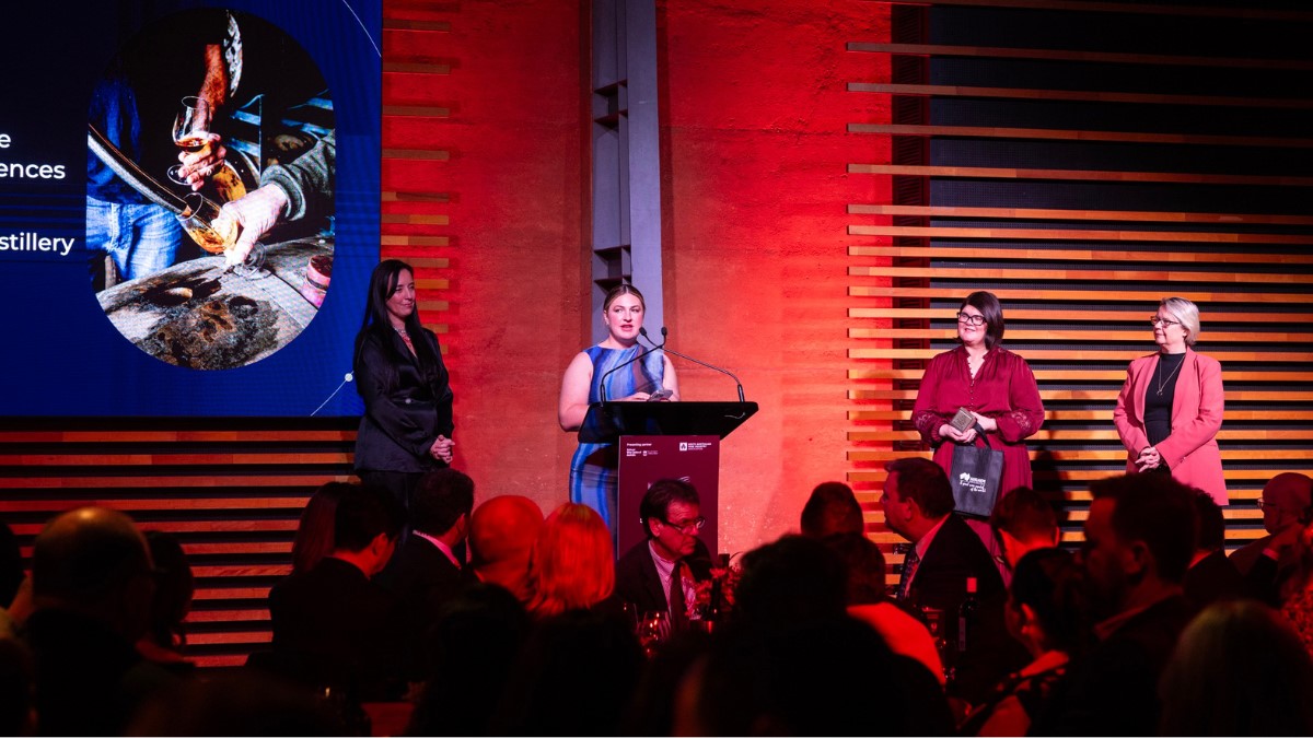 4 women on stage with one at a microphone speaking after winning an award